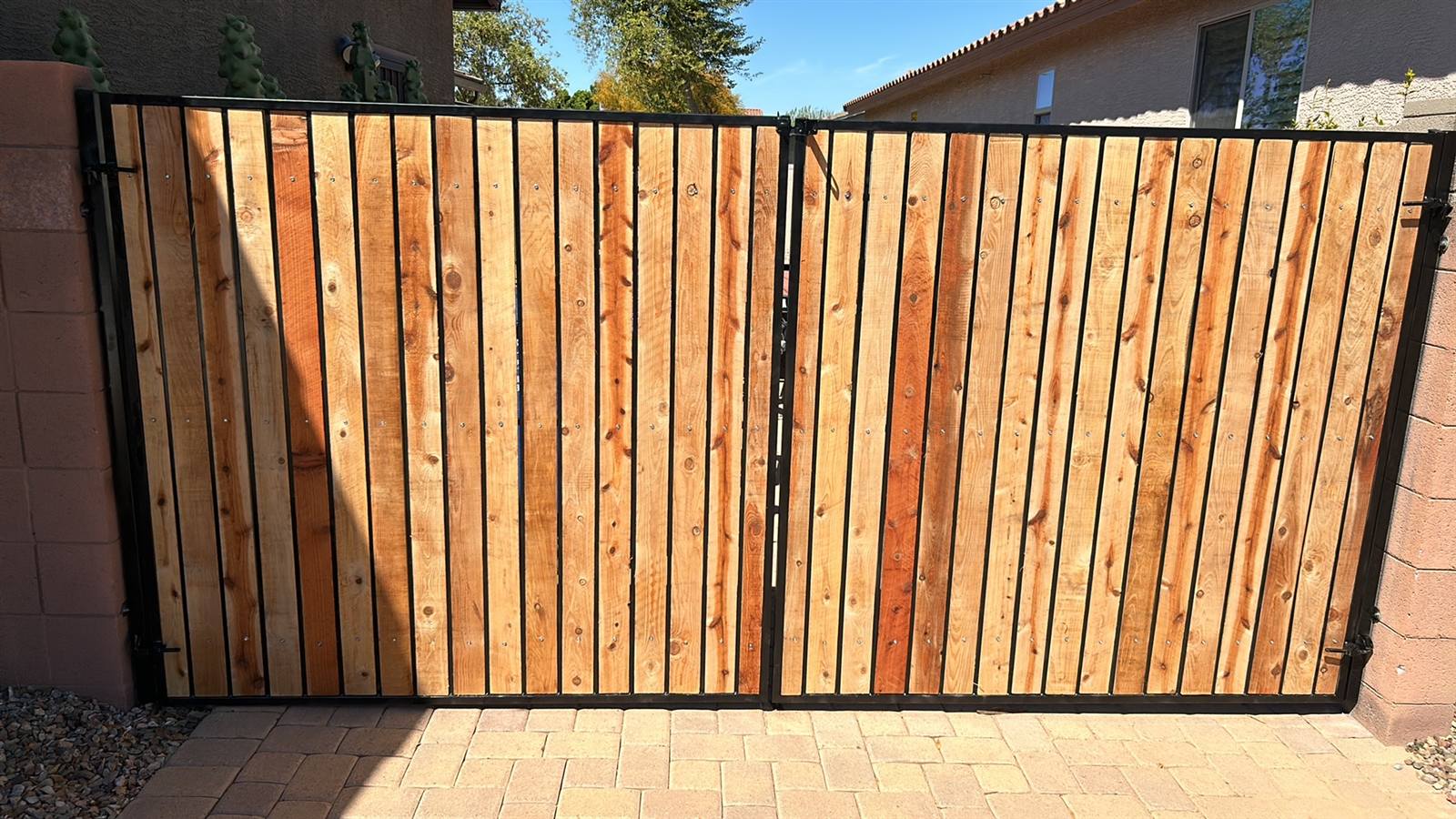 The same double driveway gate after refurbishment with clear-sealed natural cedar slats and freshly painted black frame