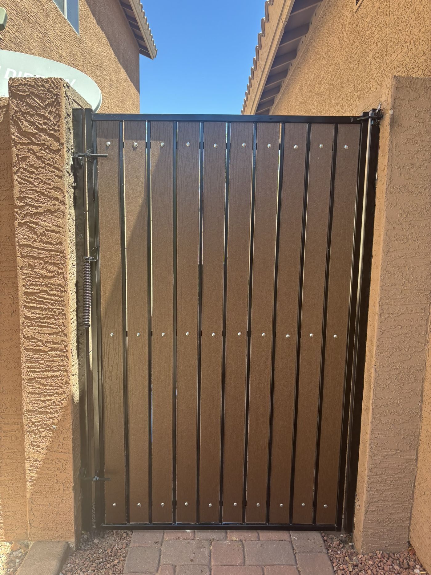 The same gate after refurbishment with rich brown composite slats, freshly painted black frame, and new bolts